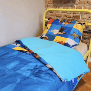 Metade superior de uma cama de solteiro com a capa de edredon, a fronha e o lençol de baixo do kit Mar de Brincar